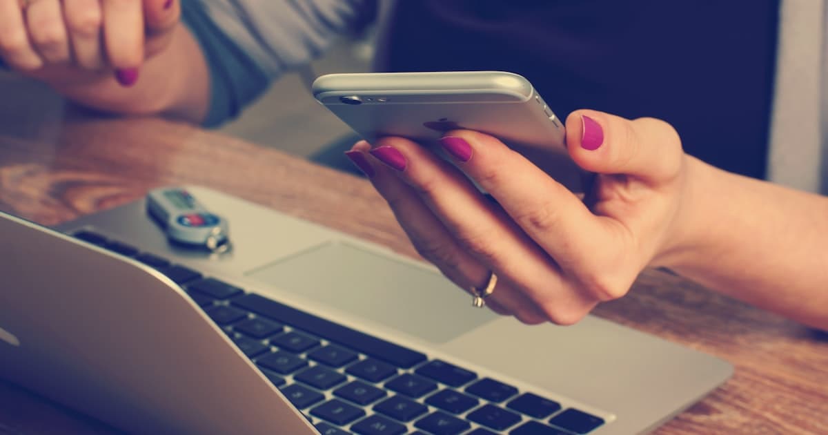 Person holding smartphone near laptop at desk